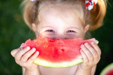 Closeup Portrait Of Cute Little Girl Eating Watermelon On The Gr Mädchen mit Wassermelone - Obst mit sehr wenigen Kohlenhydraten